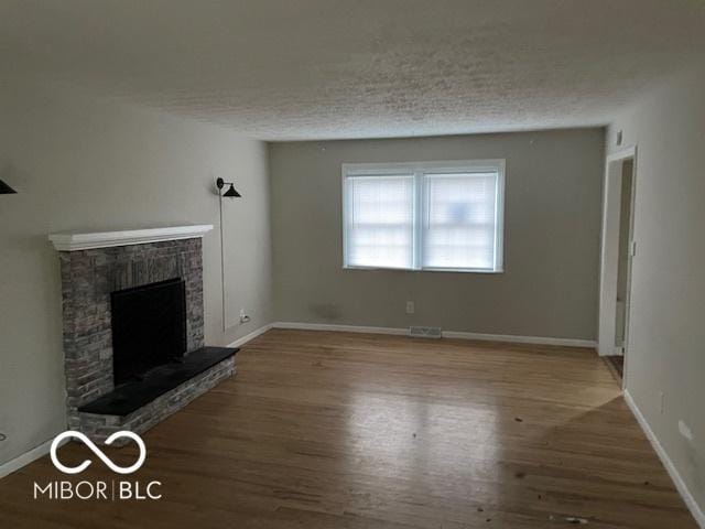 unfurnished living room featuring a fireplace, wood-type flooring, and a textured ceiling