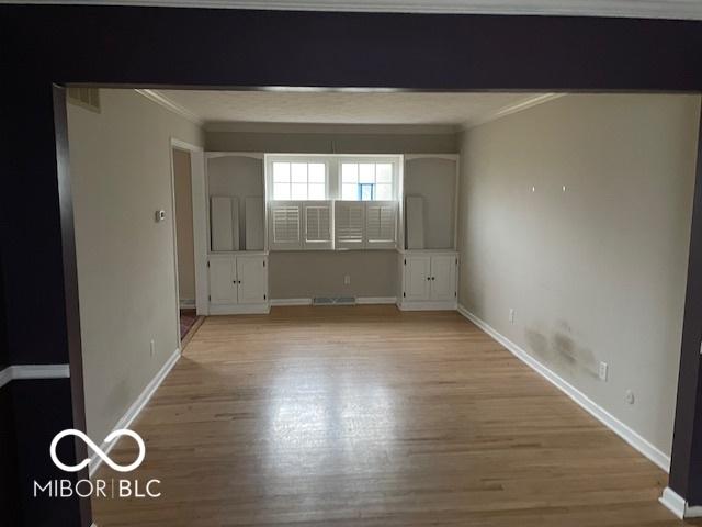 empty room with crown molding and light wood-type flooring