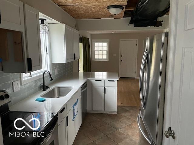 kitchen with kitchen peninsula, backsplash, stainless steel appliances, sink, and white cabinets