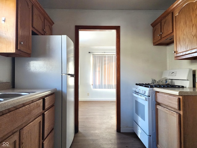 kitchen with white appliances, baseboards, dark wood-style flooring, light countertops, and brown cabinets