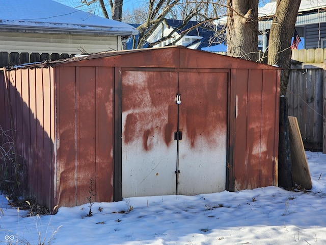 snow covered structure with an outbuilding, fence, and a shed