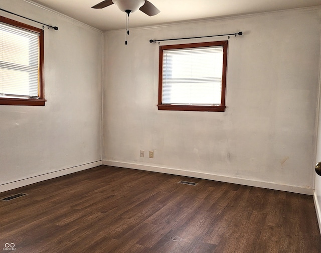 empty room featuring visible vents, plenty of natural light, dark wood-type flooring, and crown molding