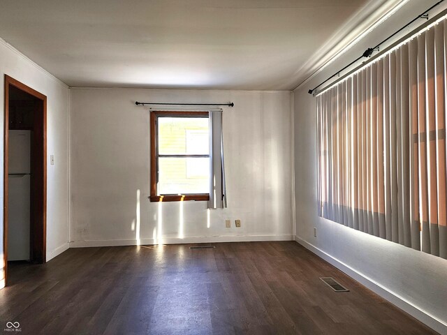 empty room featuring visible vents, baseboards, dark wood finished floors, and ornamental molding