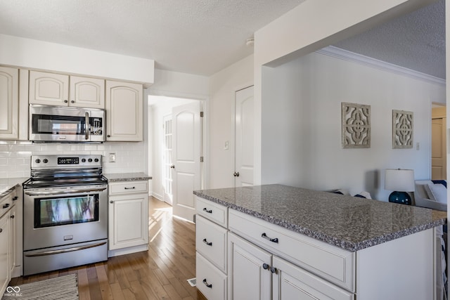 kitchen featuring a textured ceiling, appliances with stainless steel finishes, dark hardwood / wood-style flooring, dark stone counters, and tasteful backsplash