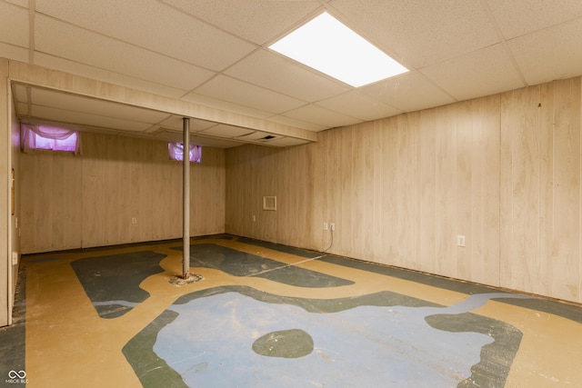 basement with a drop ceiling and wooden walls