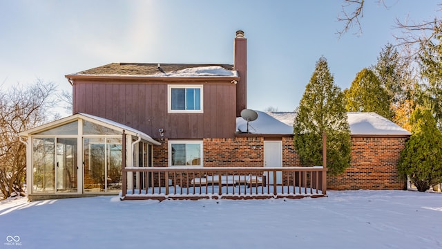 snow covered rear of property with a sunroom