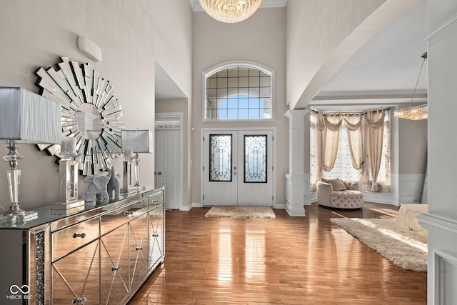 entryway featuring french doors, an inviting chandelier, hardwood / wood-style flooring, decorative columns, and a high ceiling