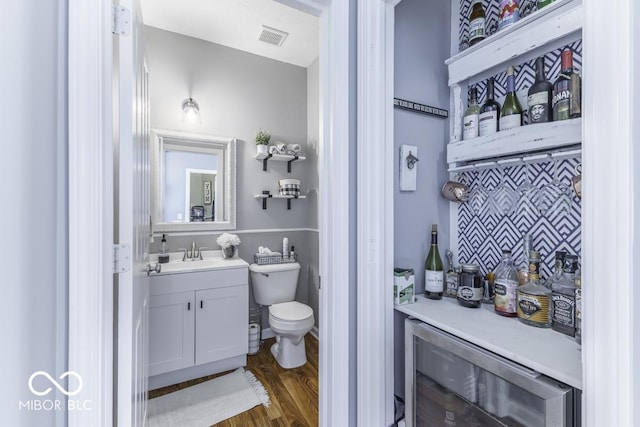 bathroom featuring wine cooler, vanity, toilet, and hardwood / wood-style flooring