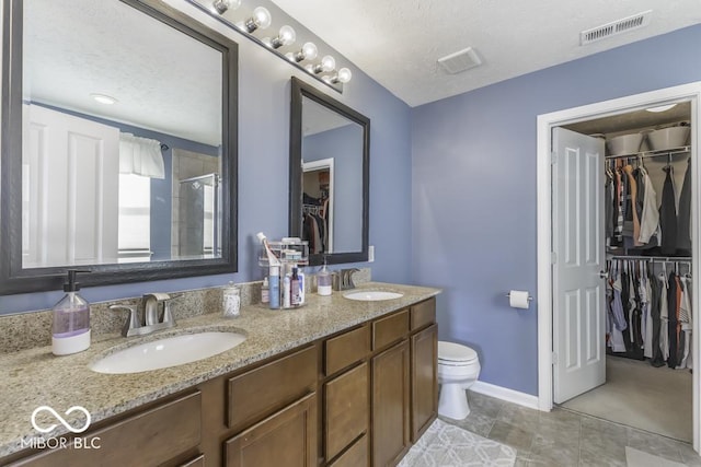 bathroom with vanity, a shower with door, toilet, and a textured ceiling