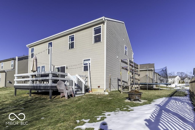 rear view of house with a wooden deck, an outdoor fire pit, a trampoline, and a lawn