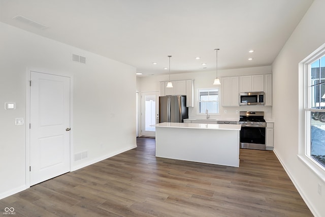 kitchen featuring appliances with stainless steel finishes, plenty of natural light, decorative light fixtures, white cabinets, and a center island