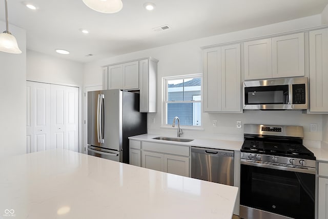 kitchen featuring appliances with stainless steel finishes, sink, light stone counters, and pendant lighting