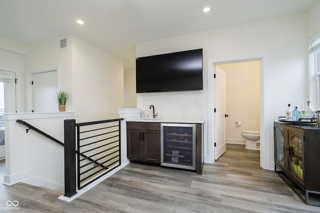 bar with beverage cooler, dark brown cabinetry, light hardwood / wood-style flooring, and sink