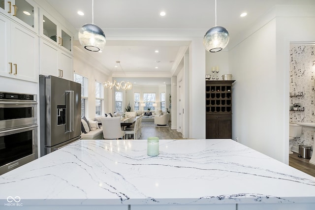 kitchen with stainless steel appliances, crown molding, light stone counters, white cabinets, and decorative light fixtures