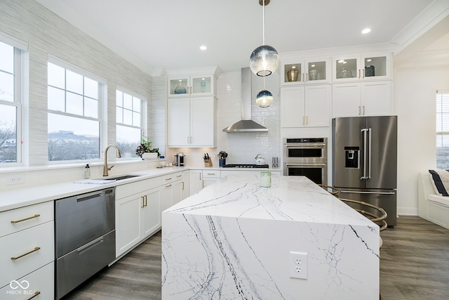 kitchen featuring wall chimney exhaust hood, pendant lighting, a kitchen island, white cabinets, and appliances with stainless steel finishes