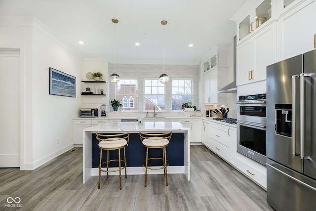 kitchen featuring stainless steel appliances, hanging light fixtures, a center island, crown molding, and white cabinetry