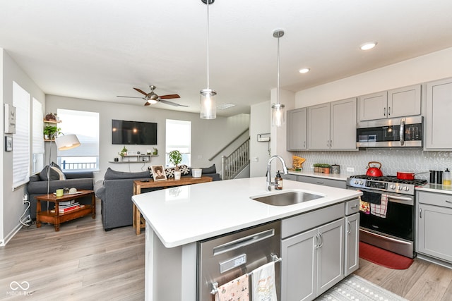 kitchen featuring gray cabinets, a center island with sink, a wealth of natural light, sink, and appliances with stainless steel finishes