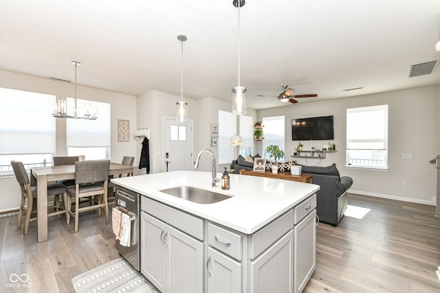 kitchen with light hardwood / wood-style floors, sink, hanging light fixtures, a kitchen island with sink, and ceiling fan with notable chandelier