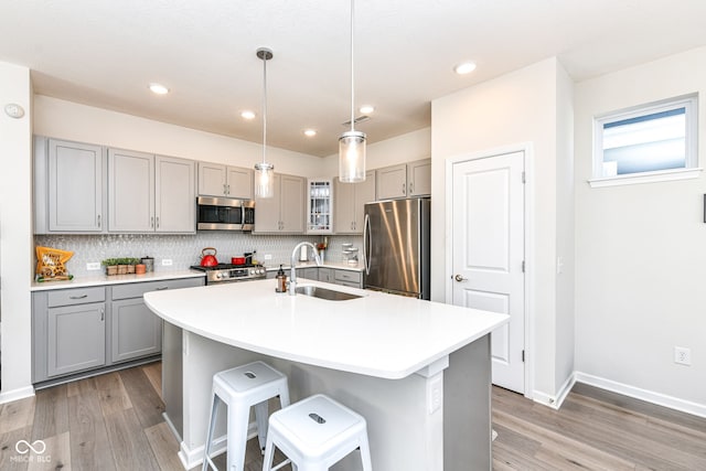 kitchen with an island with sink, appliances with stainless steel finishes, sink, and gray cabinetry