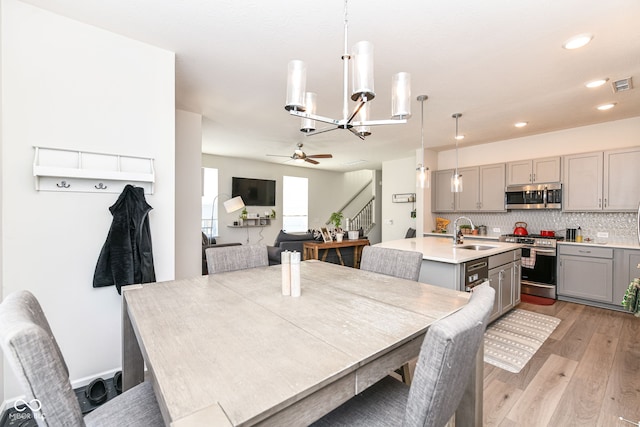 dining space featuring sink, ceiling fan with notable chandelier, and light hardwood / wood-style flooring