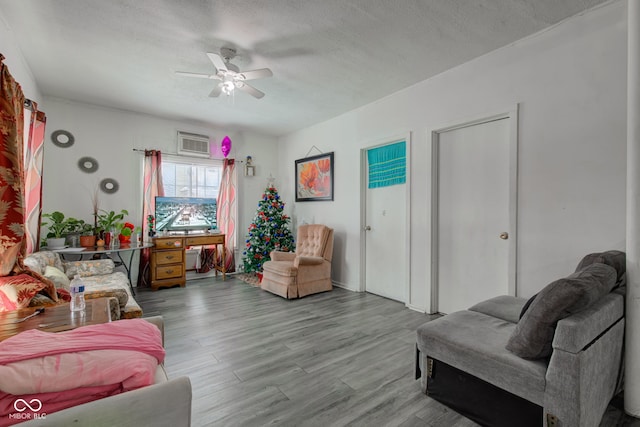 living room featuring ceiling fan, a wall mounted AC, light hardwood / wood-style floors, and a textured ceiling