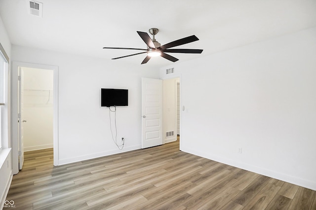 unfurnished bedroom featuring ceiling fan, a walk in closet, light hardwood / wood-style flooring, and a closet