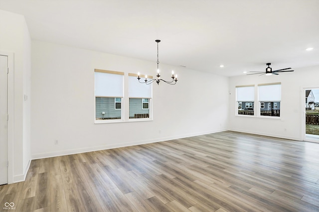 spare room with ceiling fan with notable chandelier, a healthy amount of sunlight, and light hardwood / wood-style flooring