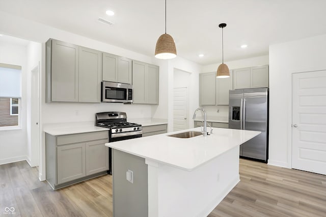 kitchen featuring stainless steel appliances, sink, decorative light fixtures, gray cabinets, and a center island with sink