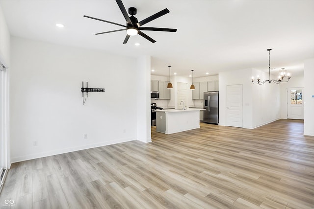 unfurnished living room with ceiling fan with notable chandelier and light hardwood / wood-style floors