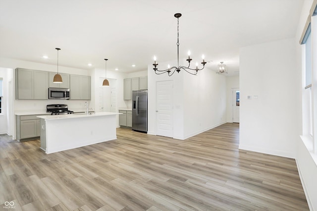 kitchen featuring hanging light fixtures, an island with sink, gray cabinetry, appliances with stainless steel finishes, and sink