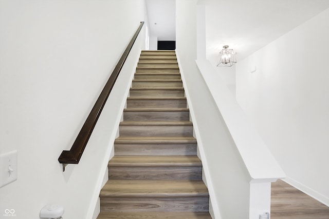 stairway with hardwood / wood-style flooring and a notable chandelier