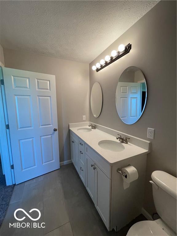 bathroom with tile patterned flooring, vanity, toilet, and a textured ceiling