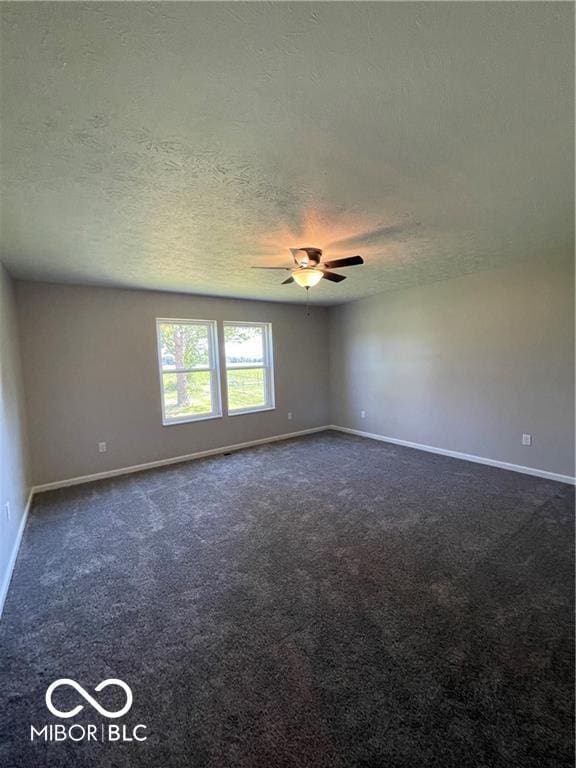 spare room with a textured ceiling, dark carpet, and ceiling fan