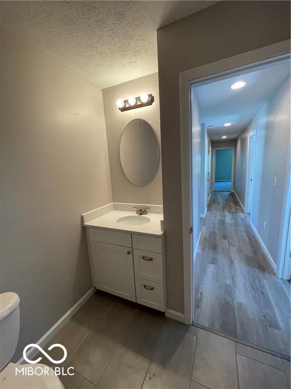 bathroom featuring vanity, wood-type flooring, a textured ceiling, and toilet