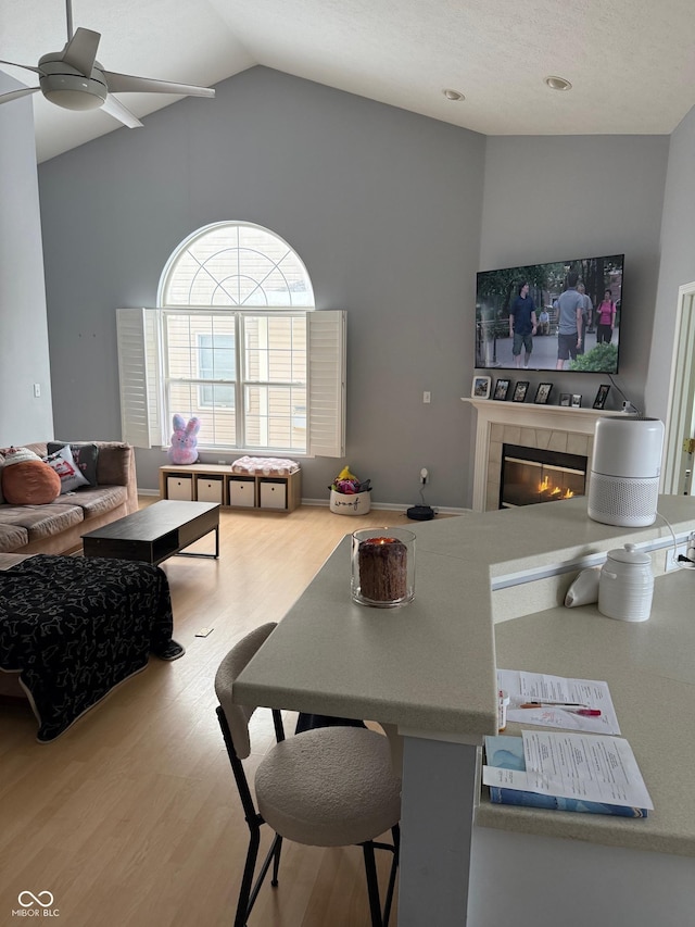 living room with a tile fireplace, ceiling fan, hardwood / wood-style floors, and lofted ceiling