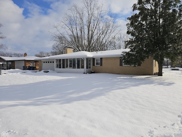 snow covered back of property with a sunroom and a garage