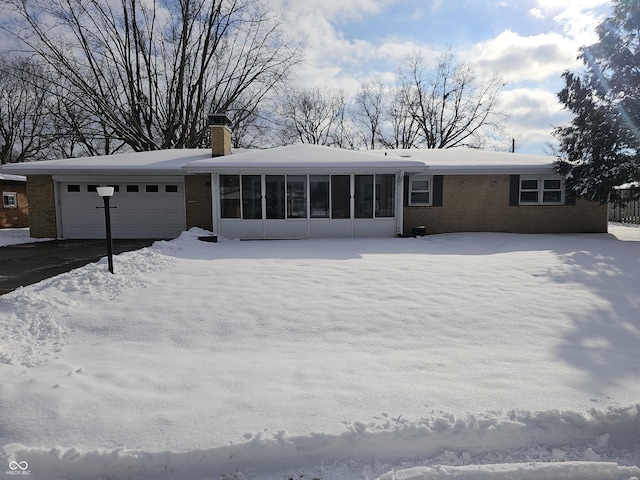 snow covered back of property with a sunroom and a garage