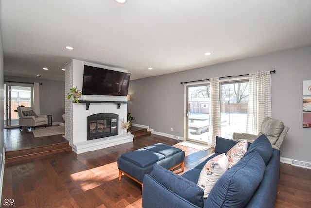 living room featuring a brick fireplace and dark wood-type flooring