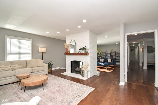 living room with a brick fireplace and dark wood-type flooring