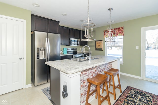 kitchen with pendant lighting, stainless steel appliances, an island with sink, a notable chandelier, and sink