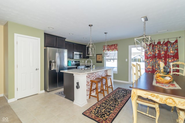 kitchen featuring appliances with stainless steel finishes, hanging light fixtures, an island with sink, a breakfast bar, and light stone counters