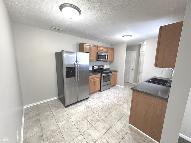 kitchen featuring sink, light tile patterned flooring, stainless steel appliances, and a textured ceiling