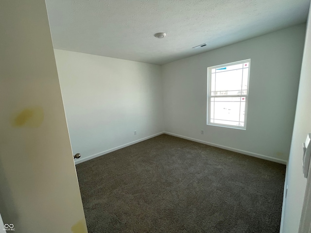 spare room featuring dark colored carpet and a textured ceiling