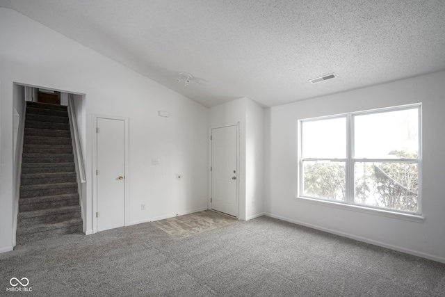 carpeted spare room with vaulted ceiling and a textured ceiling