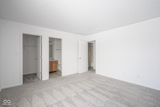 unfurnished bedroom with a closet, a textured ceiling, connected bathroom, a walk in closet, and light colored carpet