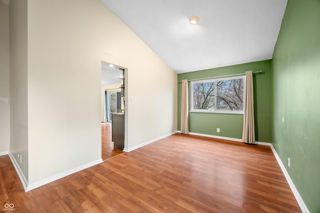 empty room featuring lofted ceiling, wood finished floors, and baseboards