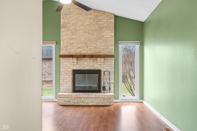 unfurnished living room featuring lofted ceiling, a brick fireplace, plenty of natural light, and wood finished floors