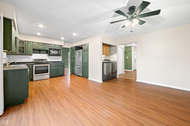 kitchen with washer / dryer, appliances with stainless steel finishes, green cabinets, and light wood-style floors