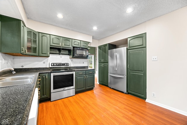 kitchen featuring stainless steel appliances, a sink, green cabinets, light wood finished floors, and tasteful backsplash