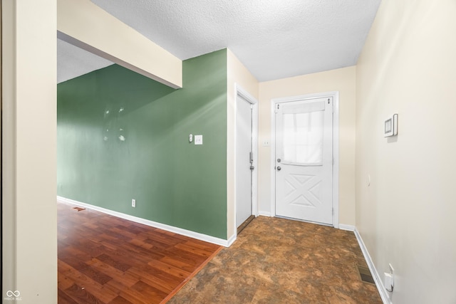 foyer entrance featuring a textured ceiling, wood finished floors, visible vents, and baseboards